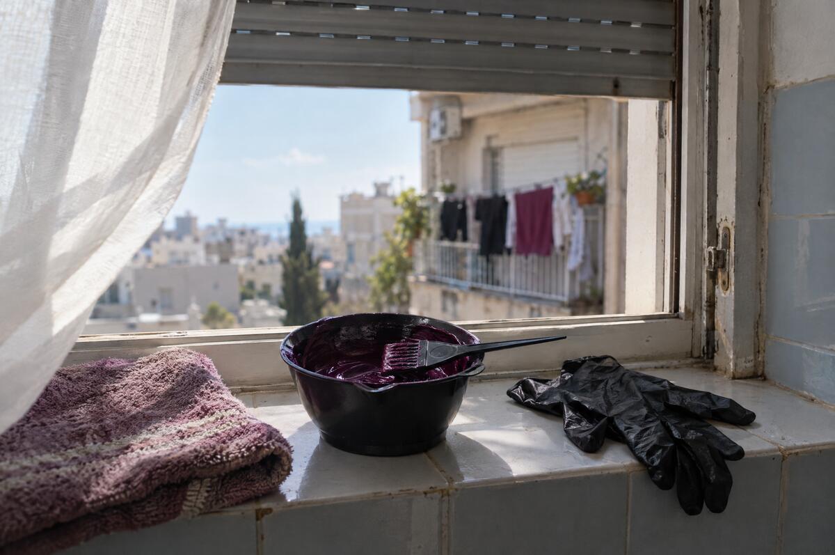 קערית עם צבע שיער סגול, מברשת צביעה וכפפות על אדן חלון פתוח בבוקר